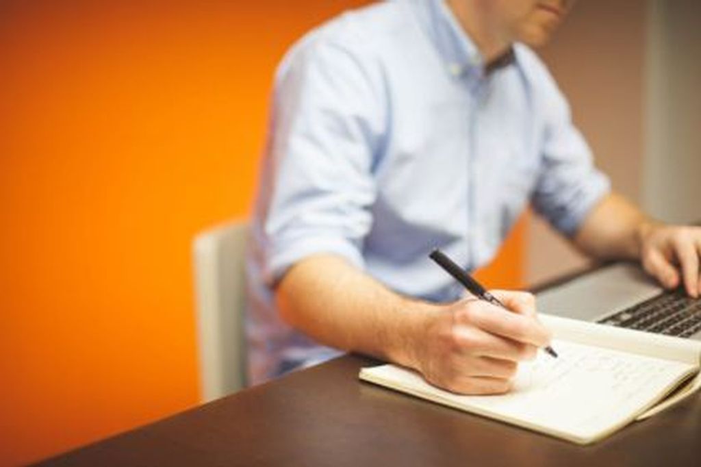 Pessoa fazendo anotações em um caderno enquanto usa um laptop, representa busca e orçamento quanto custa para comprar um diploma de curso técnico de forma legítima e reconhecida.